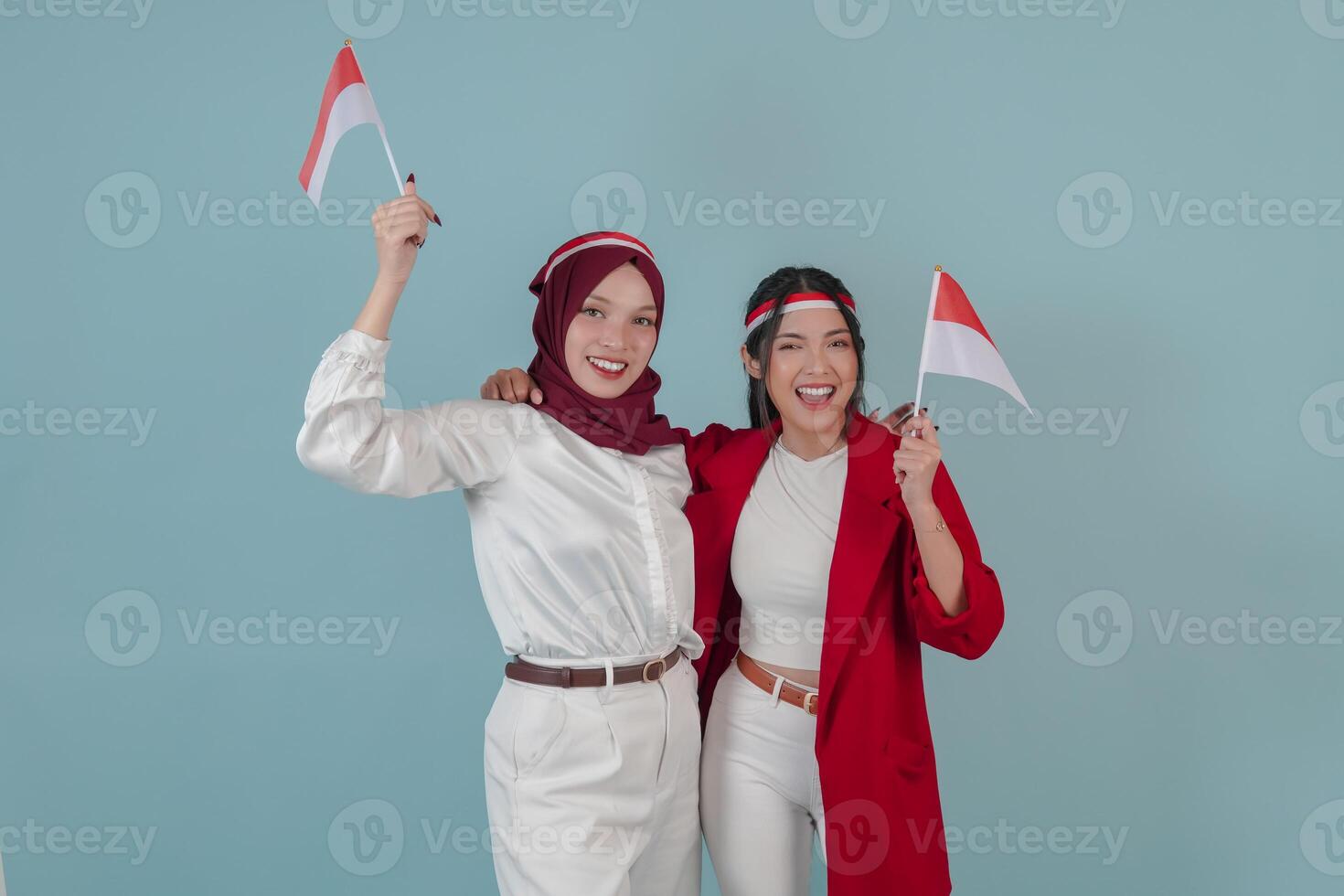 Two joyful Indonesian women holding mini country flag smiling and posing for a photo. photo