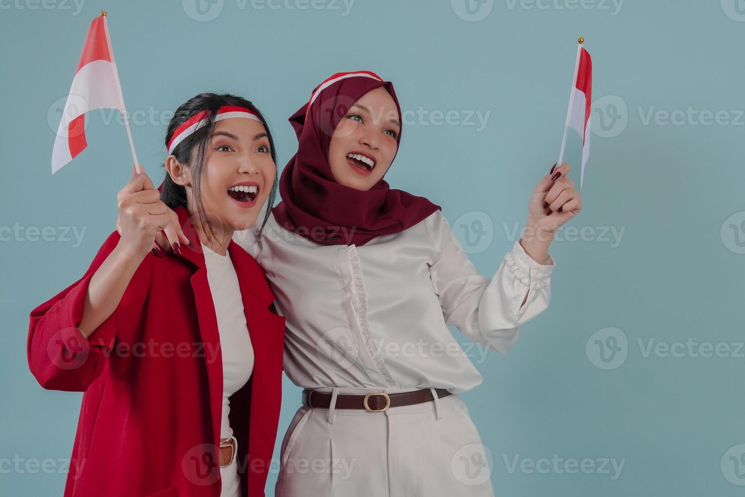 Two excited Indonesian women holding mini country flag smiling and giving support. photo