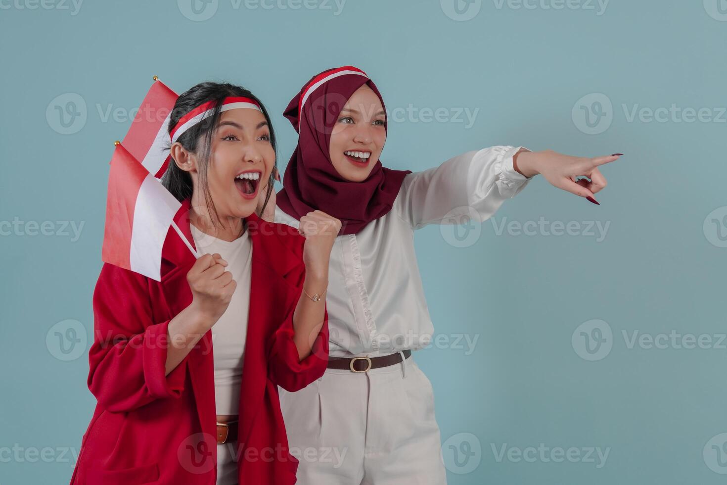 Two young Indonesian women holding a mini country flag and pointing at something. photo