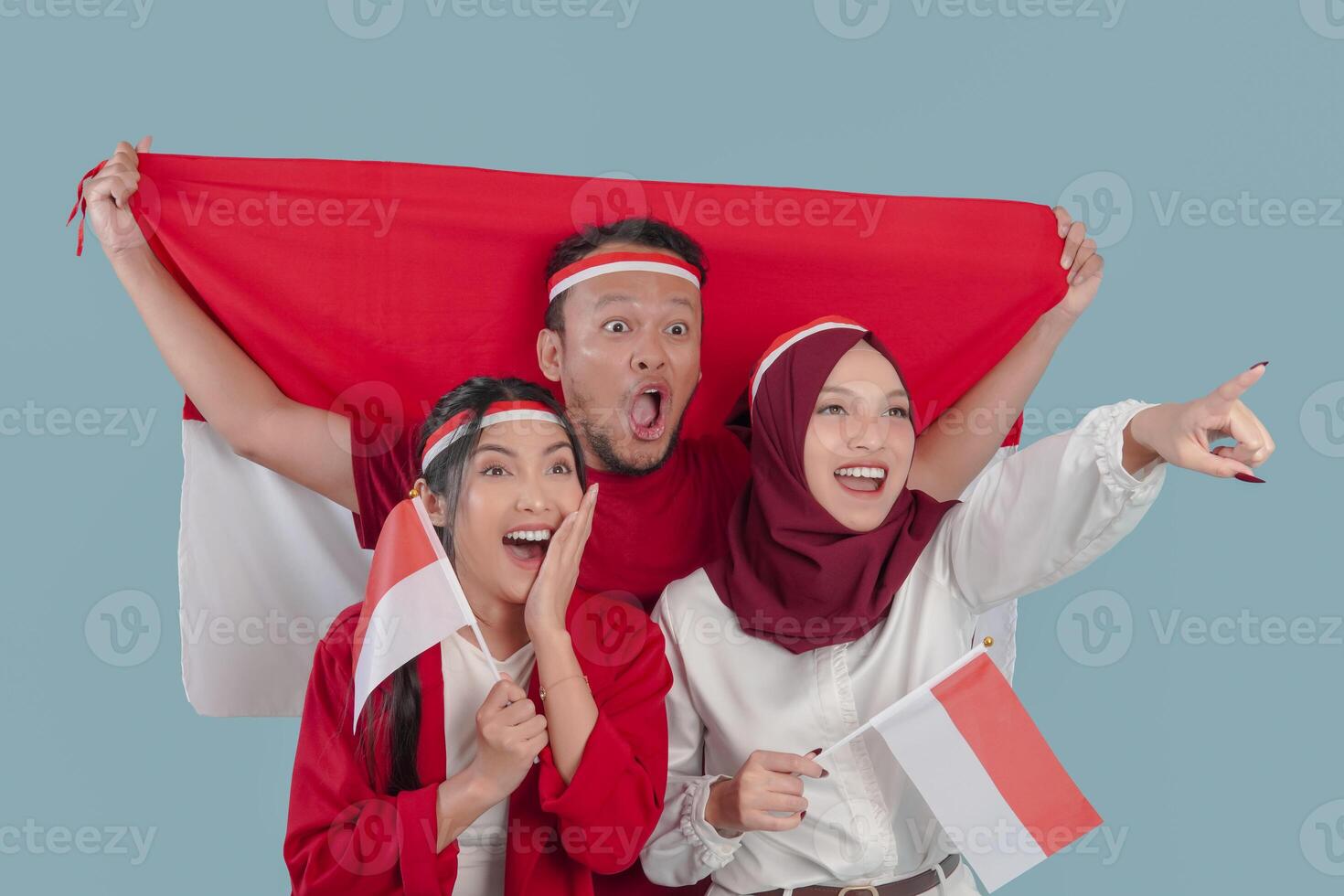Three Indonesian people are holding their country flag smiling and pointing to something. photo