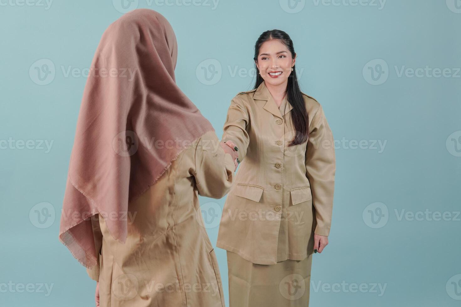 Two smiling Indonesian government worker women wearing khaki uniform doing handshake gesture. photo