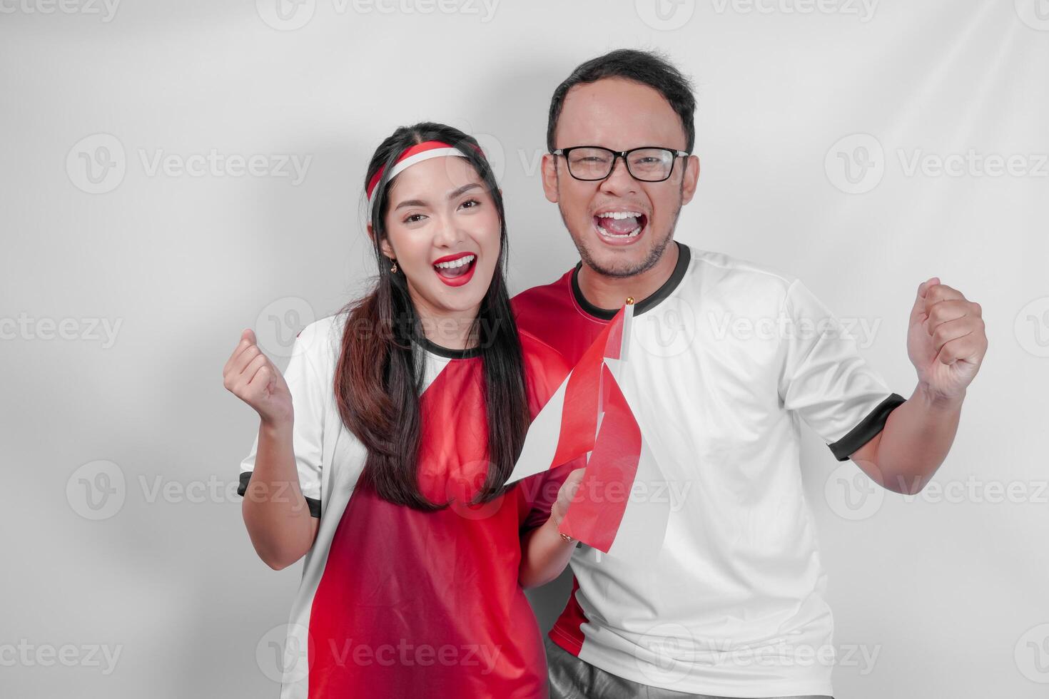 Cheerful Indonesian young couple holding flags while raising fist to support in a sport match. photo