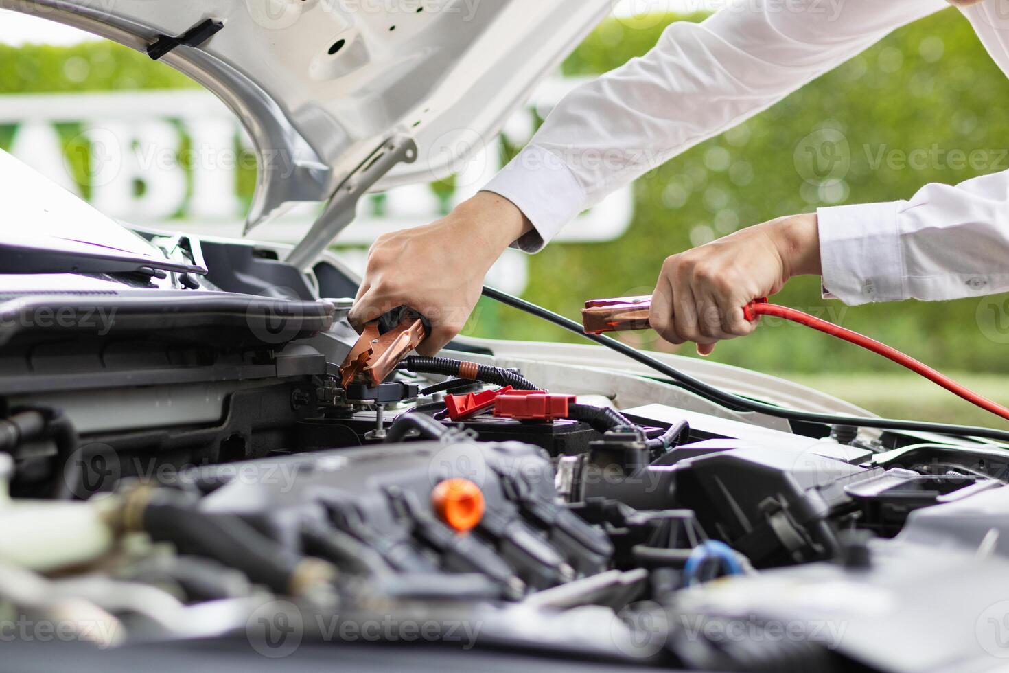 mechanic from the service center is helping to jump start the car battery for customer who has a deteriorated battery and cannot start the car. Jump starting the battery helps to continue the journey photo
