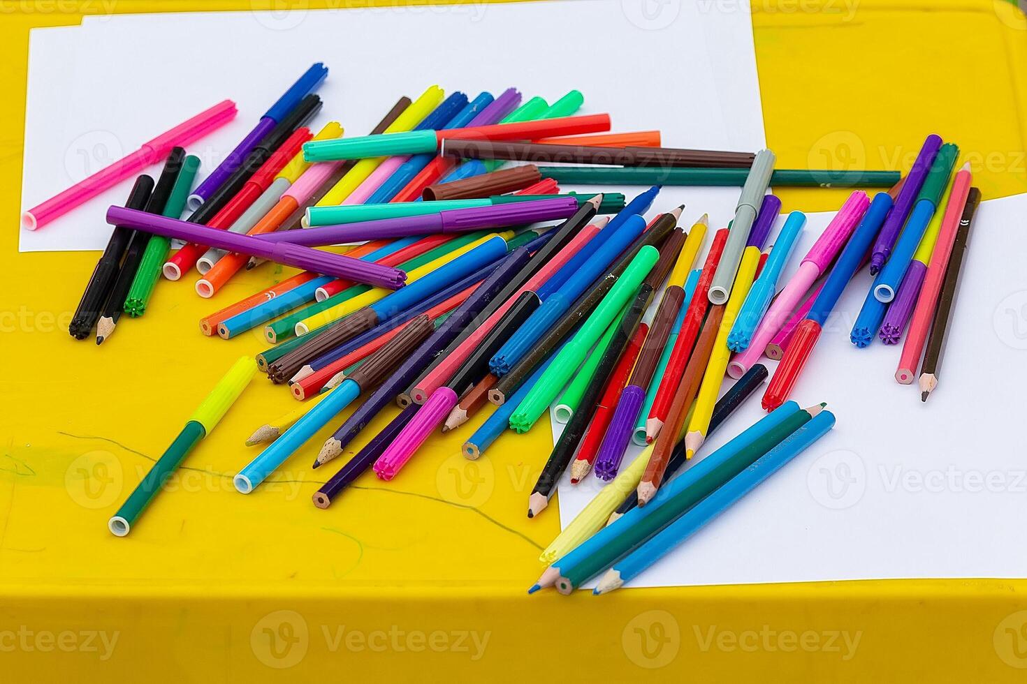 Multi-colored pencils, felt-tip pens, sheets of white paper on the table photo