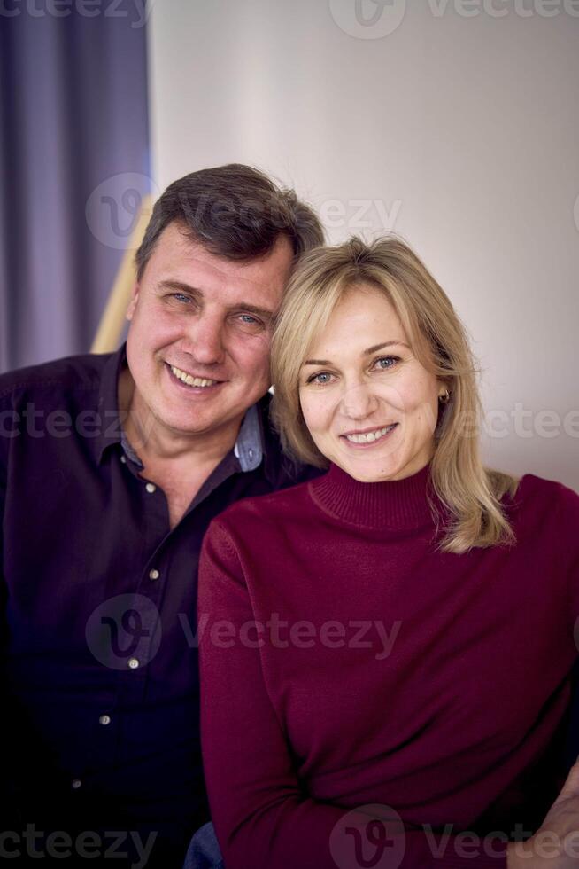 attractive middle-aged married couple hugging and smiling on sofa, studio photo shoot