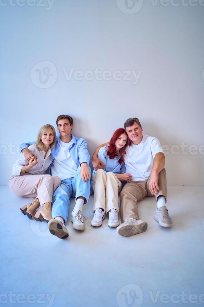 a family, middle-aged husband and wife, young adult son and teenage daughter, sitting on a white background, studio photo shoot