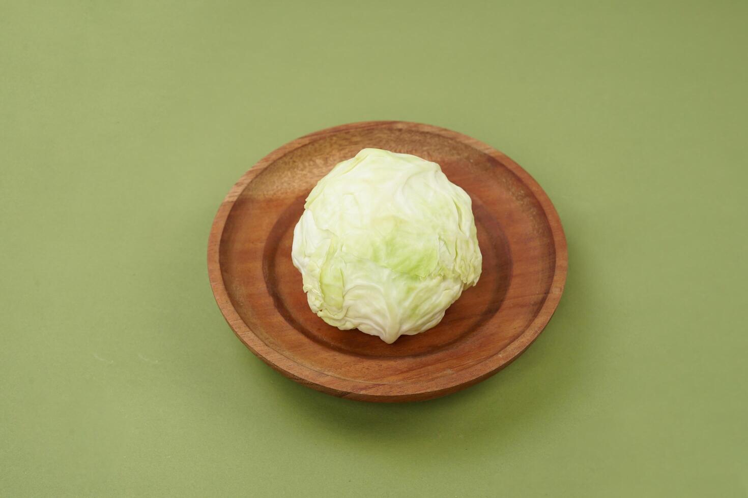 Green cabbage on a wooden plate, isolated against a green background, top view photo