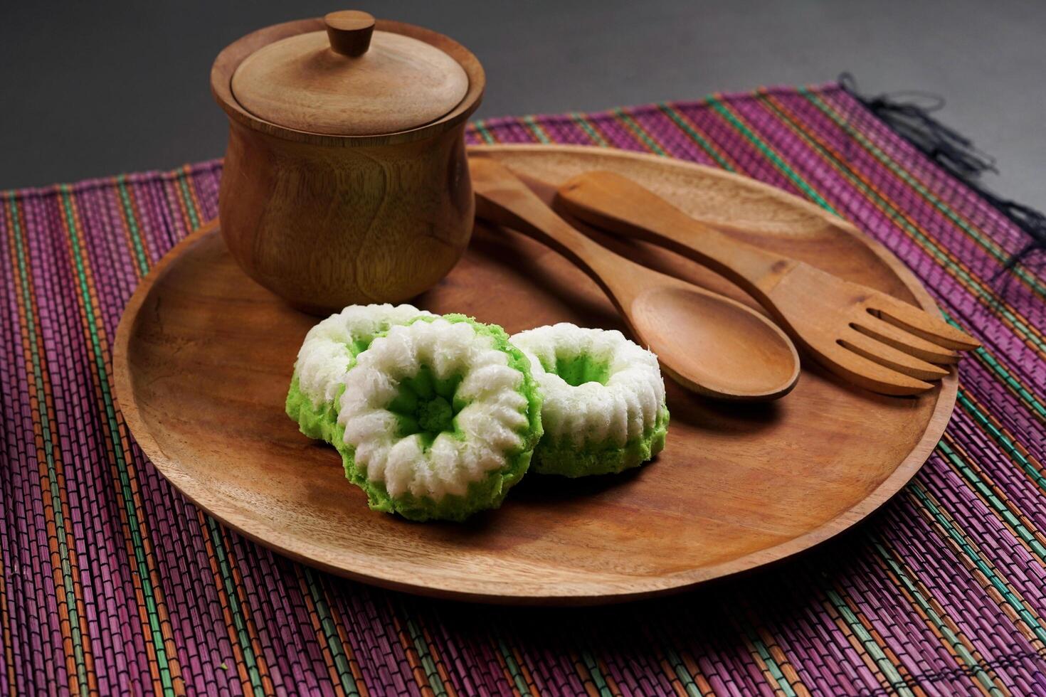 Putu Ayu is served on a wooden plate on a rainbow-colored base. It is a traditional dessert made from steamed rice flour and topped with grated coconut, a classic Indonesian cake photo