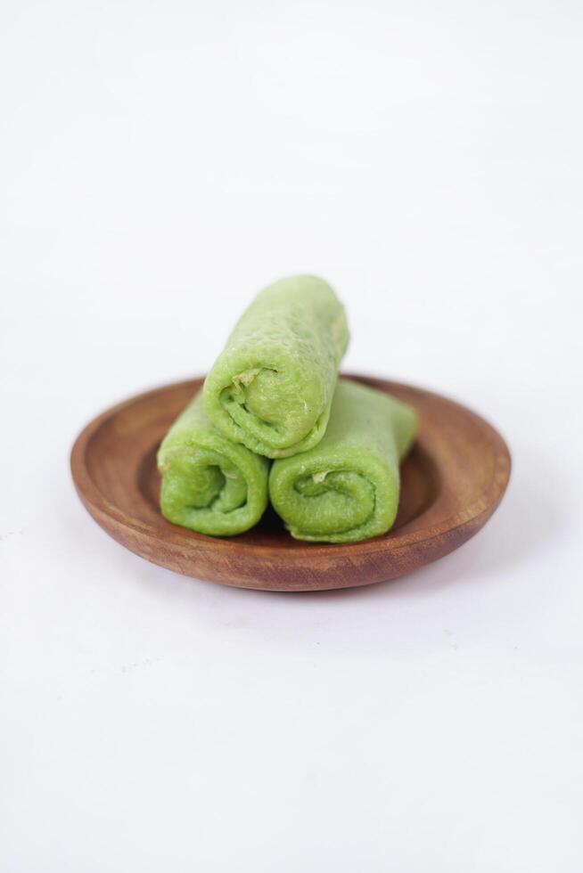 Traditional Indonesian food called 'Dadar Gulung' on a wooden plate, an elliptical cake filled with grated coconut and liquid palm sugar, isolated on a white background. photo