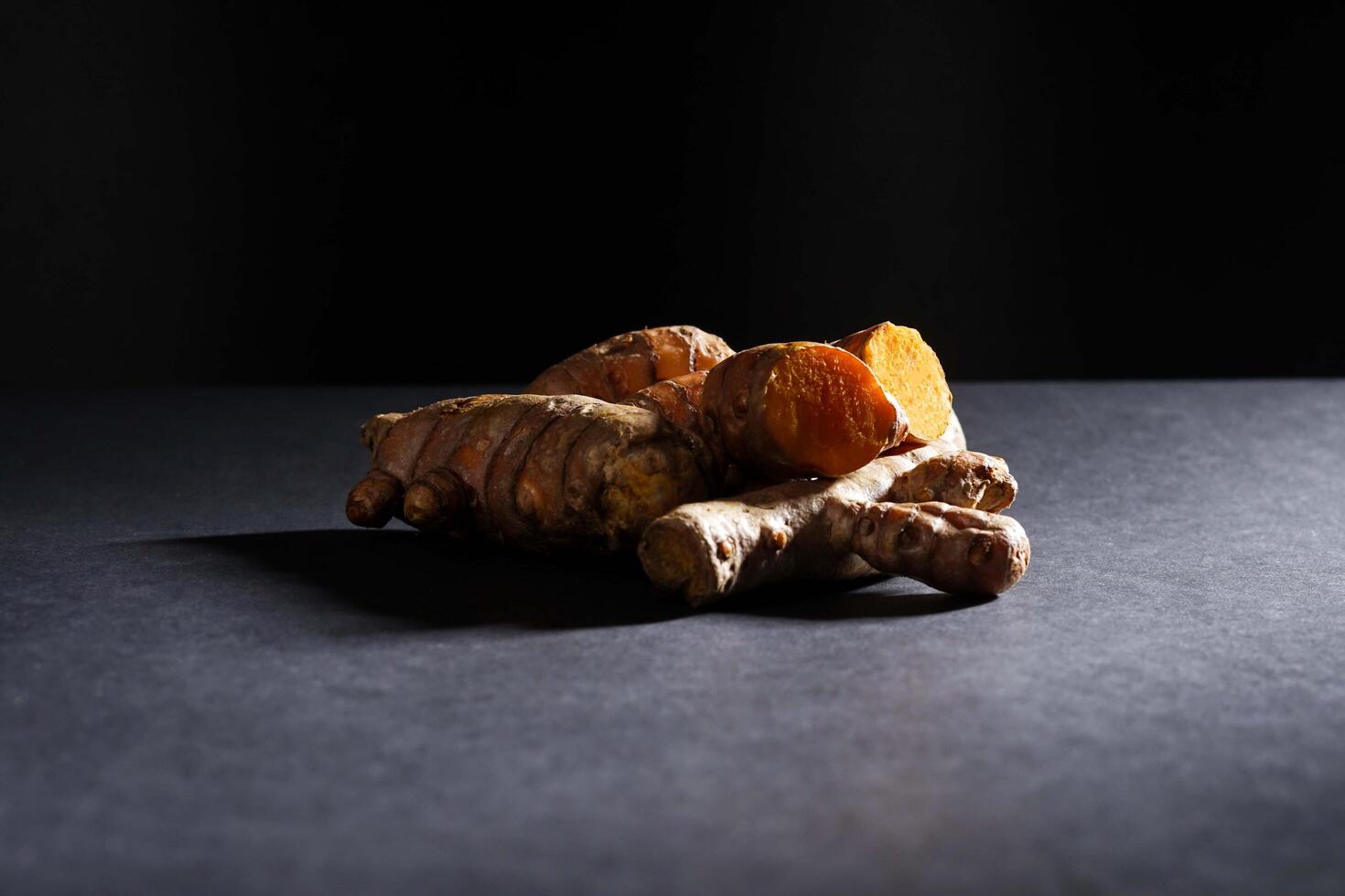 Fresh turmeric root and slices in wooden bowl isolated on dark background, turmeric Curcuma longa Linn, spice concept photo