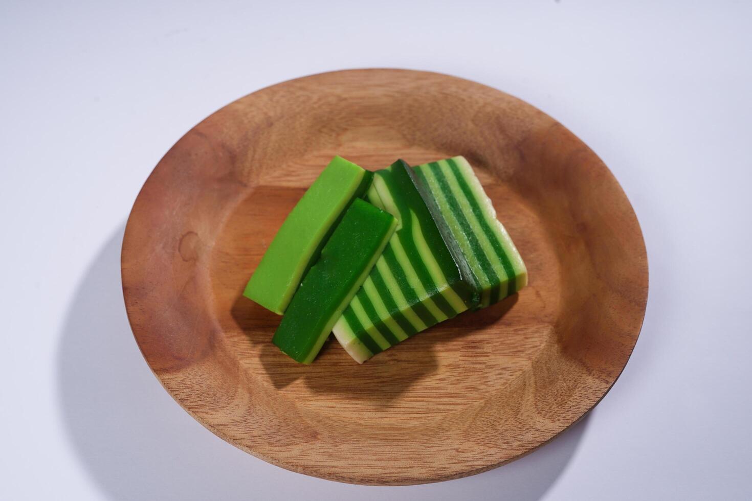 Sticky layer cake or Kue Lapis on wooden plate isolated on white background. Indonesian traditional dessert made from rice flour and coconut milk, steamed layer by layer served on banana leaves. photo