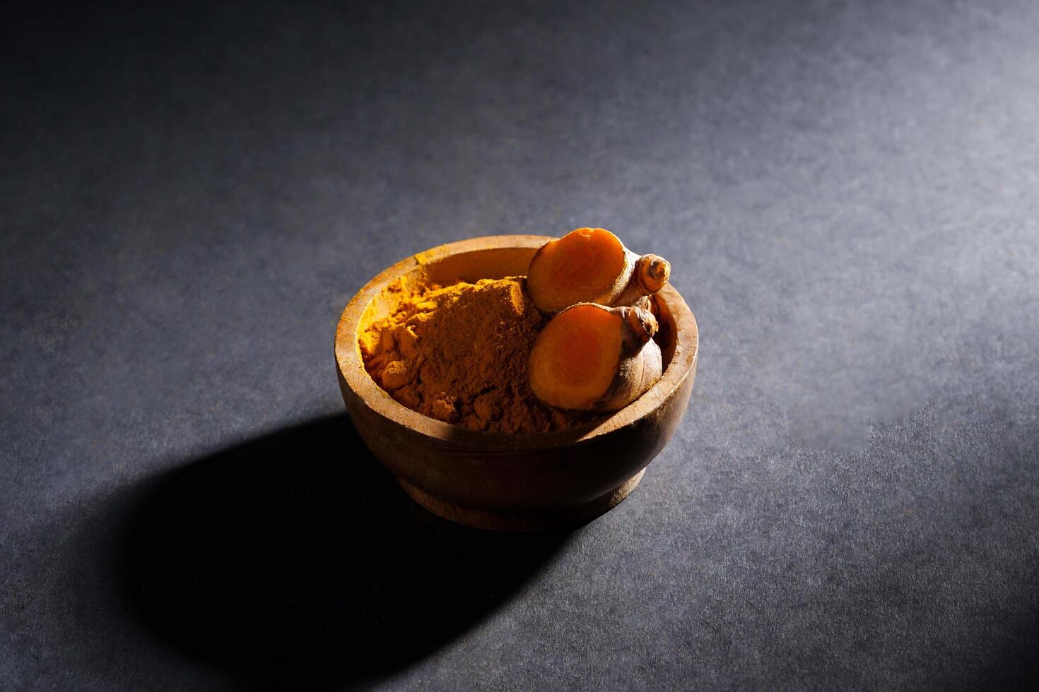 Fresh turmeric root and turmeric powder in wooden bowl, turmeric isolated on dark background, spice concept photo
