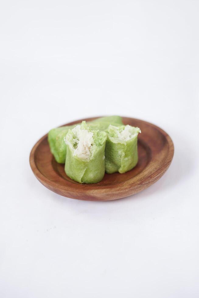 Traditional Indonesian food called 'Dadar Gulung' on a wooden plate, an elliptical cake filled with grated coconut and liquid palm sugar, isolated on a white background. photo