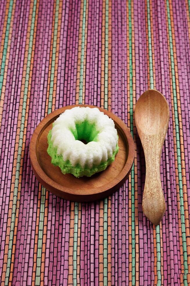 Putu Ayu is served on a wooden plate on a rainbow-colored base. It is a traditional dessert made from steamed rice flour and topped with grated coconut, a classic Indonesian cake photo