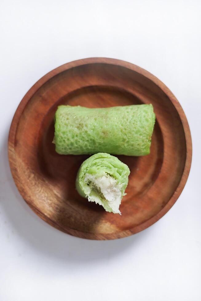Traditional Indonesian food called 'Dadar Gulung' on a wooden plate, an elliptical cake filled with grated coconut and liquid palm sugar, Dadar gulung top view isolated on a white background. photo