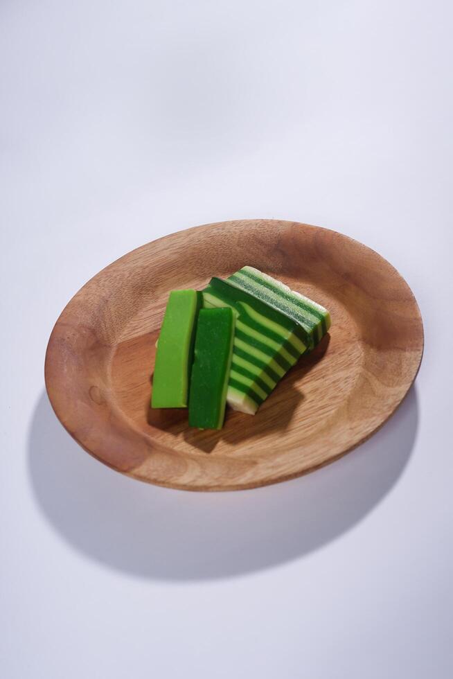 Sticky layer cake or Kue Lapis on wooden plate isolated on white background. Indonesian traditional dessert made from rice flour and coconut milk, steamed layer by layer served on banana leaves. photo