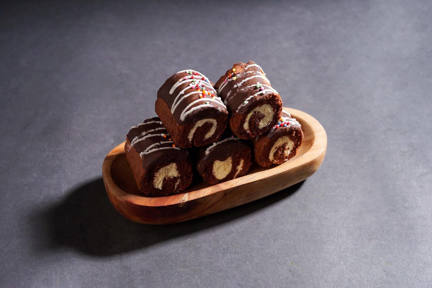 Chocolate roll cake with fresh cream in wooden plate isolated on dark background. chocolate swiss roll cake. photo