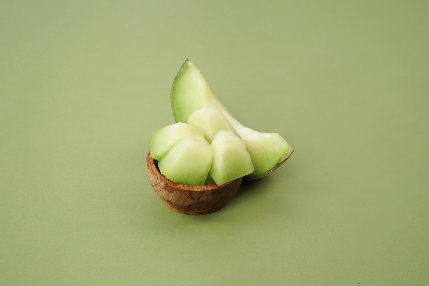 Green cantaloupe melon slice in wooden bowl isolated on green background, green melon photo