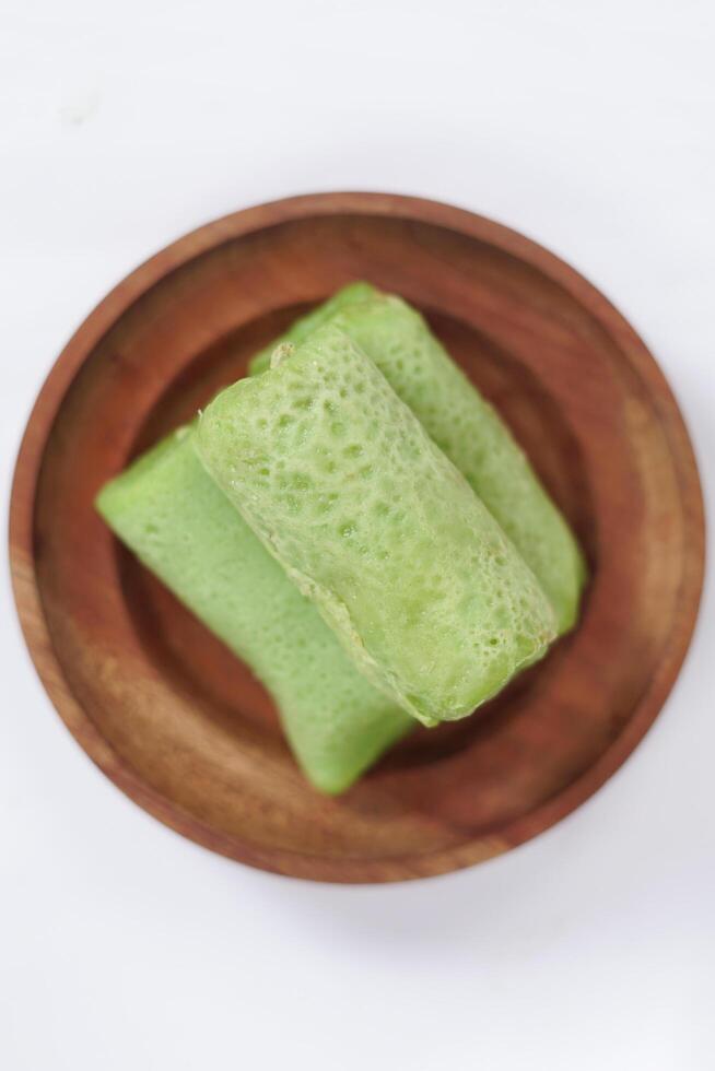 Traditional Indonesian food called 'Dadar Gulung' on a wooden plate, an elliptical cake filled with grated coconut and liquid palm sugar, Dadar gulung top view isolated on a white background. photo