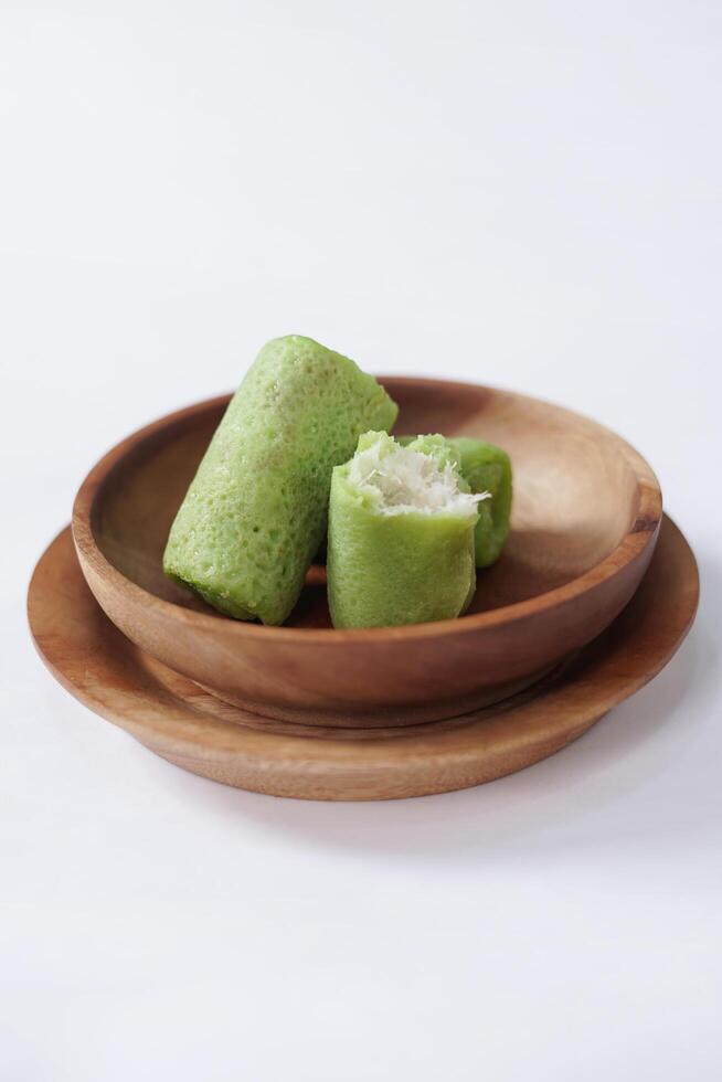 Traditional Indonesian food called 'Dadar Gulung' on a wooden plate, an elliptical cake filled with grated coconut and liquid palm sugar, isolated on a white background. photo