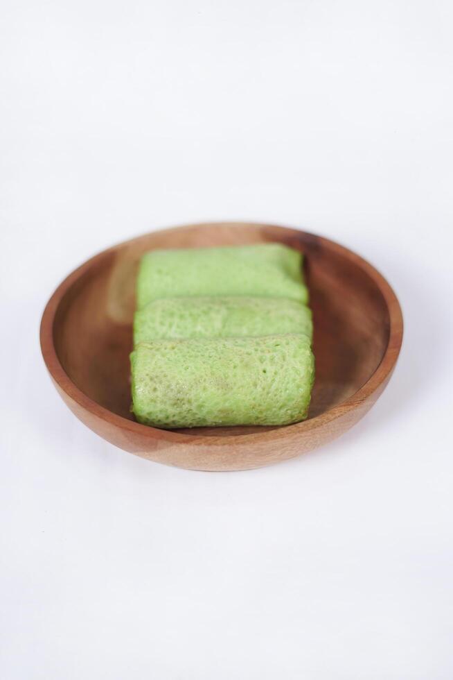 Traditional Indonesian food called 'Dadar Gulung' on a wooden plate, an elliptical cake filled with grated coconut and liquid palm sugar, isolated on a white background. photo