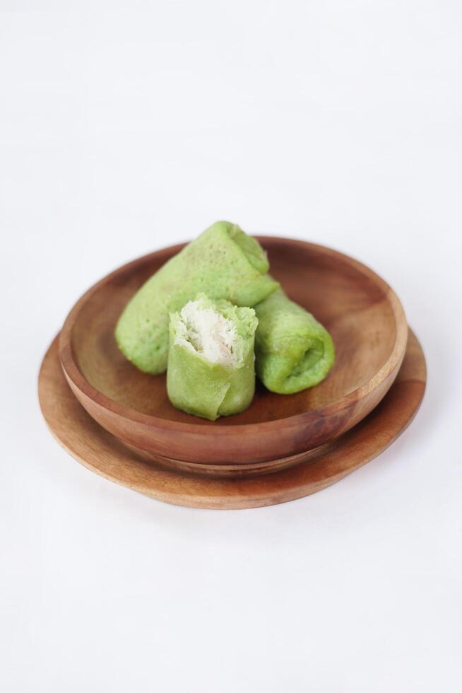 Traditional Indonesian food called 'Dadar Gulung' on a wooden plate, an elliptical cake filled with grated coconut and liquid palm sugar, isolated on a white background. photo