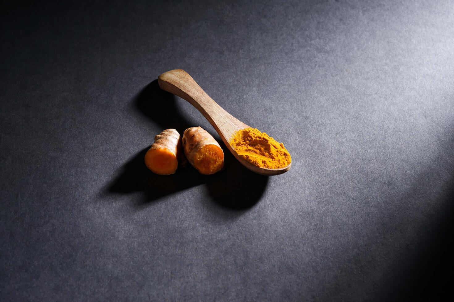Fresh turmeric root and turmeric powder in wooden spoon, turmeric isolated on dark background, spice concept photo
