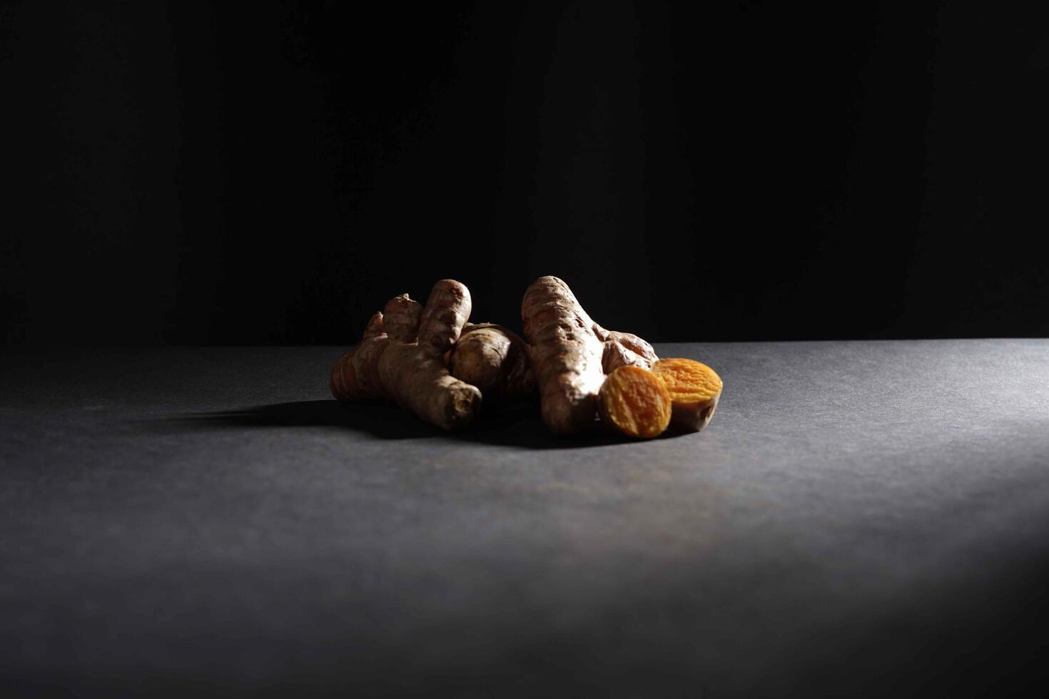 Fresh turmeric root and slices in wooden bowl isolated on dark background, turmeric Curcuma longa Linn, spice concept photo