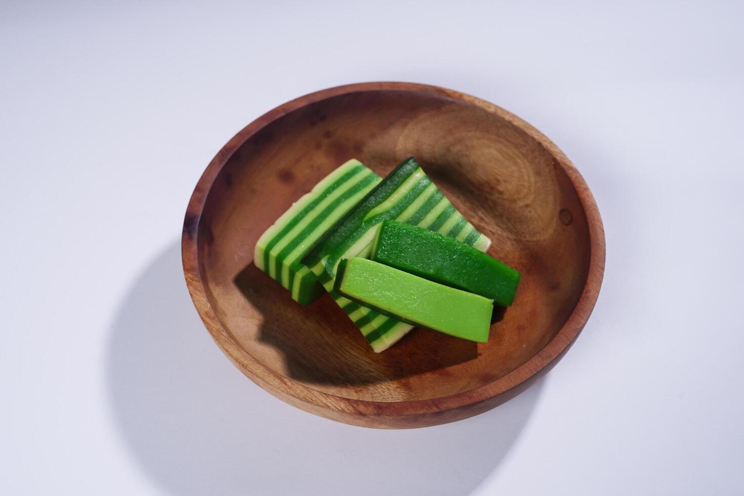 Sticky layer cake or Kue Lapis on wooden plate isolated on white background. Indonesian traditional dessert made from rice flour and coconut milk, steamed layer by layer served on banana leaves. photo
