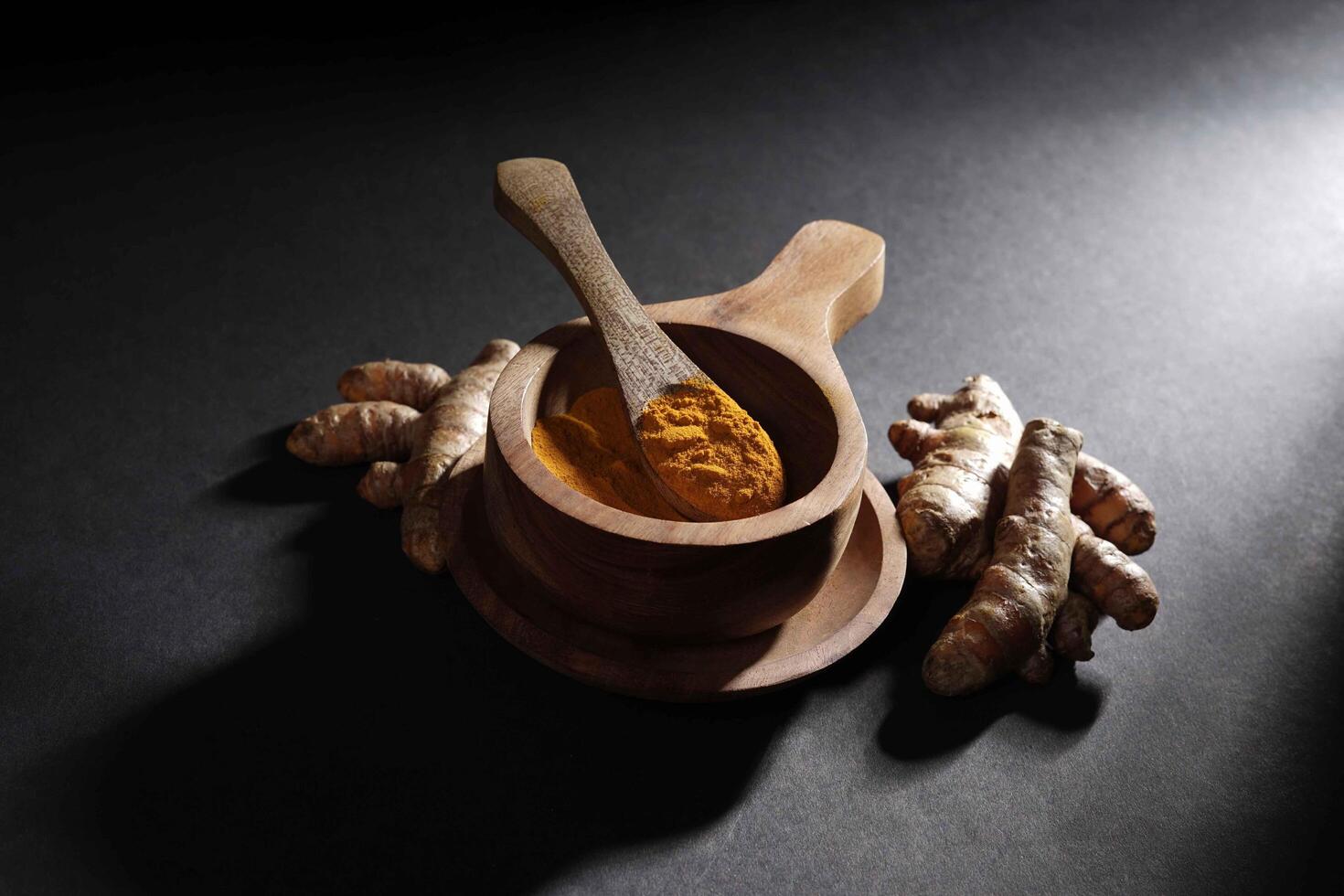 Fresh turmeric root and turmeric powder in wooden bowl, turmeric isolated on dark background, spice concept photo