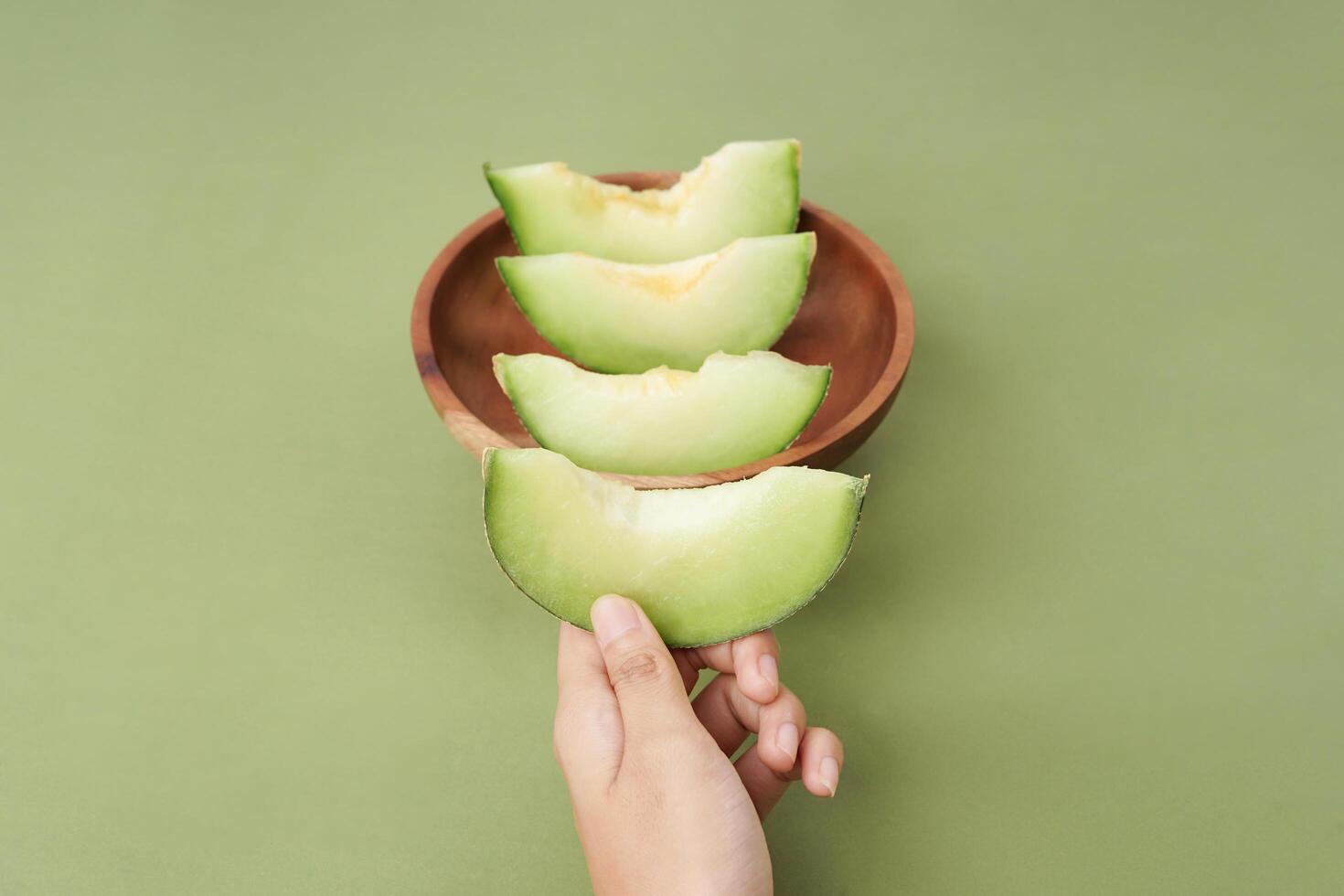 Green cantaloupe melon slice in wooden bowl isolated on green background, green melon photo