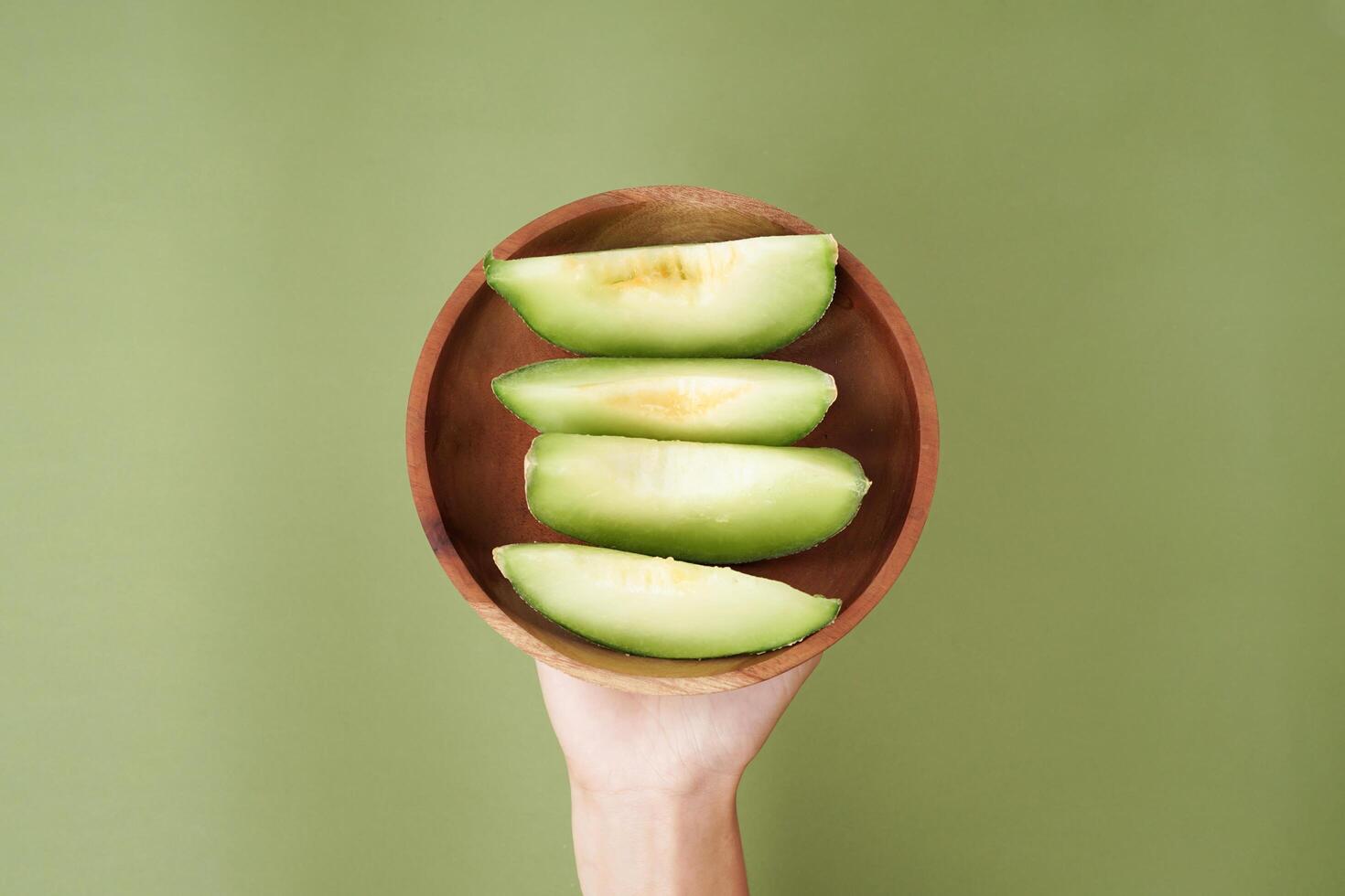 Green cantaloupe melon slice in wooden bowl isolated on green background, green melon photo