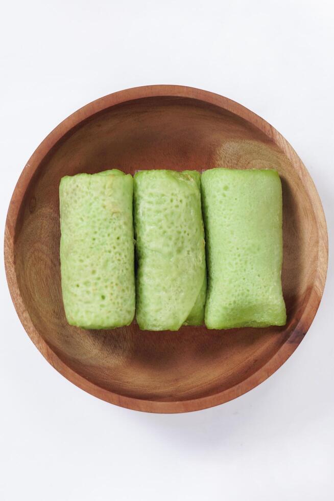 Traditional Indonesian food called 'Dadar Gulung' on a wooden plate, an elliptical cake filled with grated coconut and liquid palm sugar, Dadar gulung top view isolated on a white background. photo