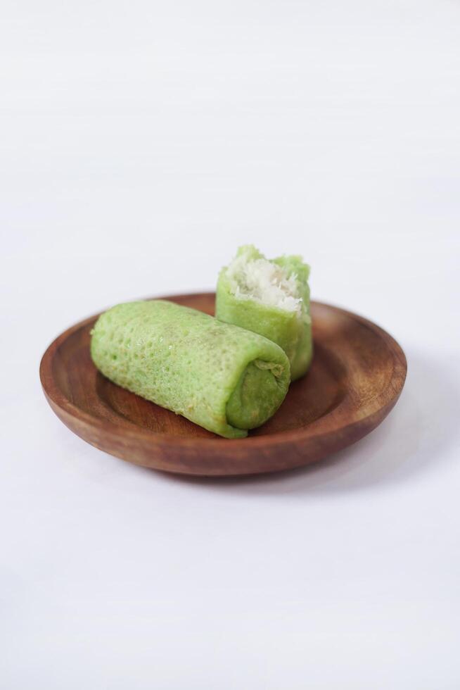 Traditional Indonesian food called 'Dadar Gulung' on a wooden plate, an elliptical cake filled with grated coconut and liquid palm sugar, isolated on a white background. photo