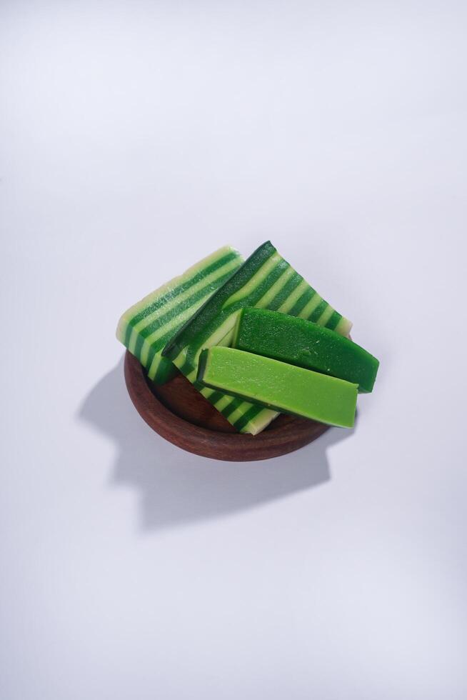 Sticky layer cake or Kue Lapis on wooden plate isolated on white background. Indonesian traditional dessert made from rice flour and coconut milk, steamed layer by layer served on banana leaves. photo