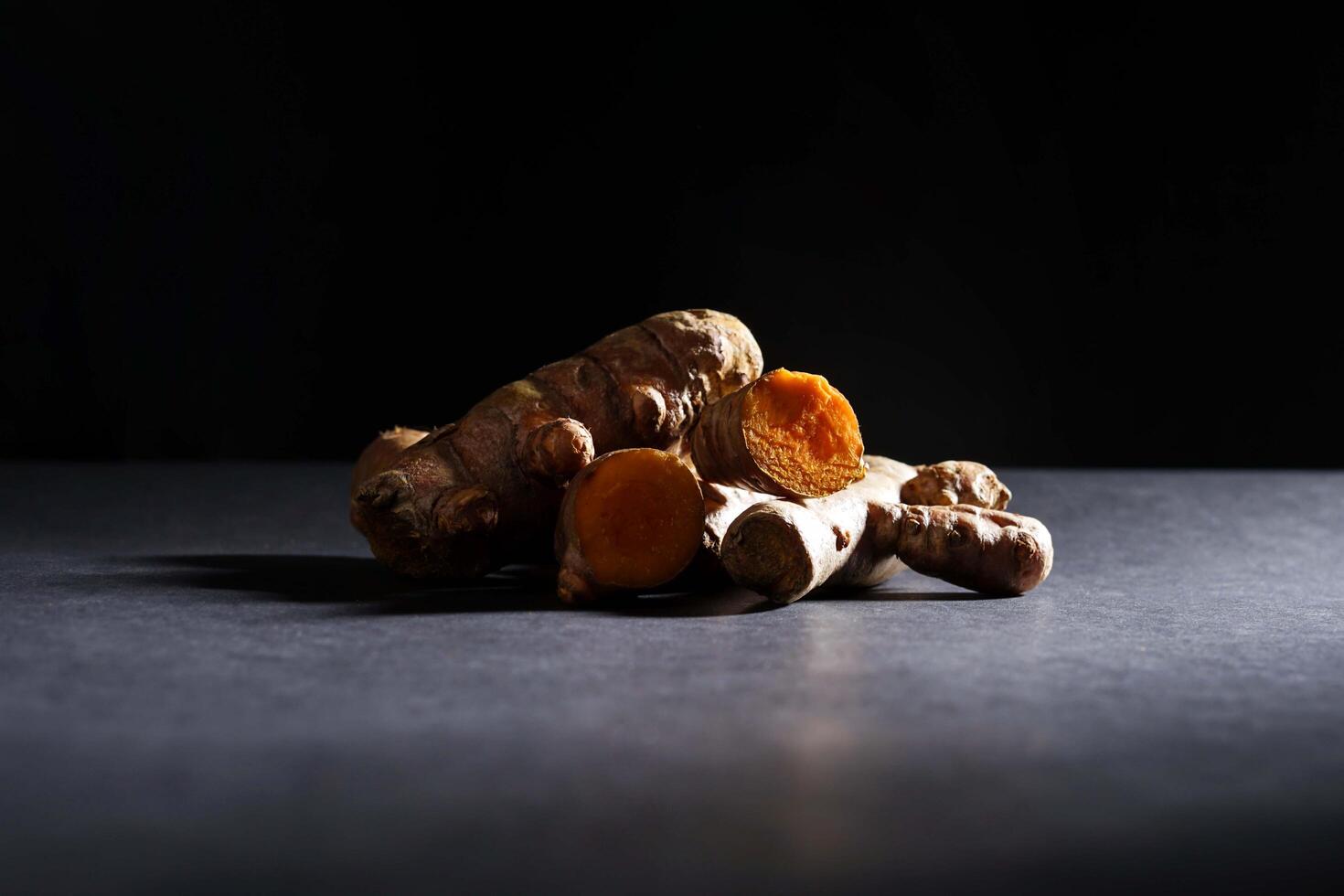 fresh turmeric root and slices isolated on dark background, turmeric Curcuma longa Linn, spice concept photo