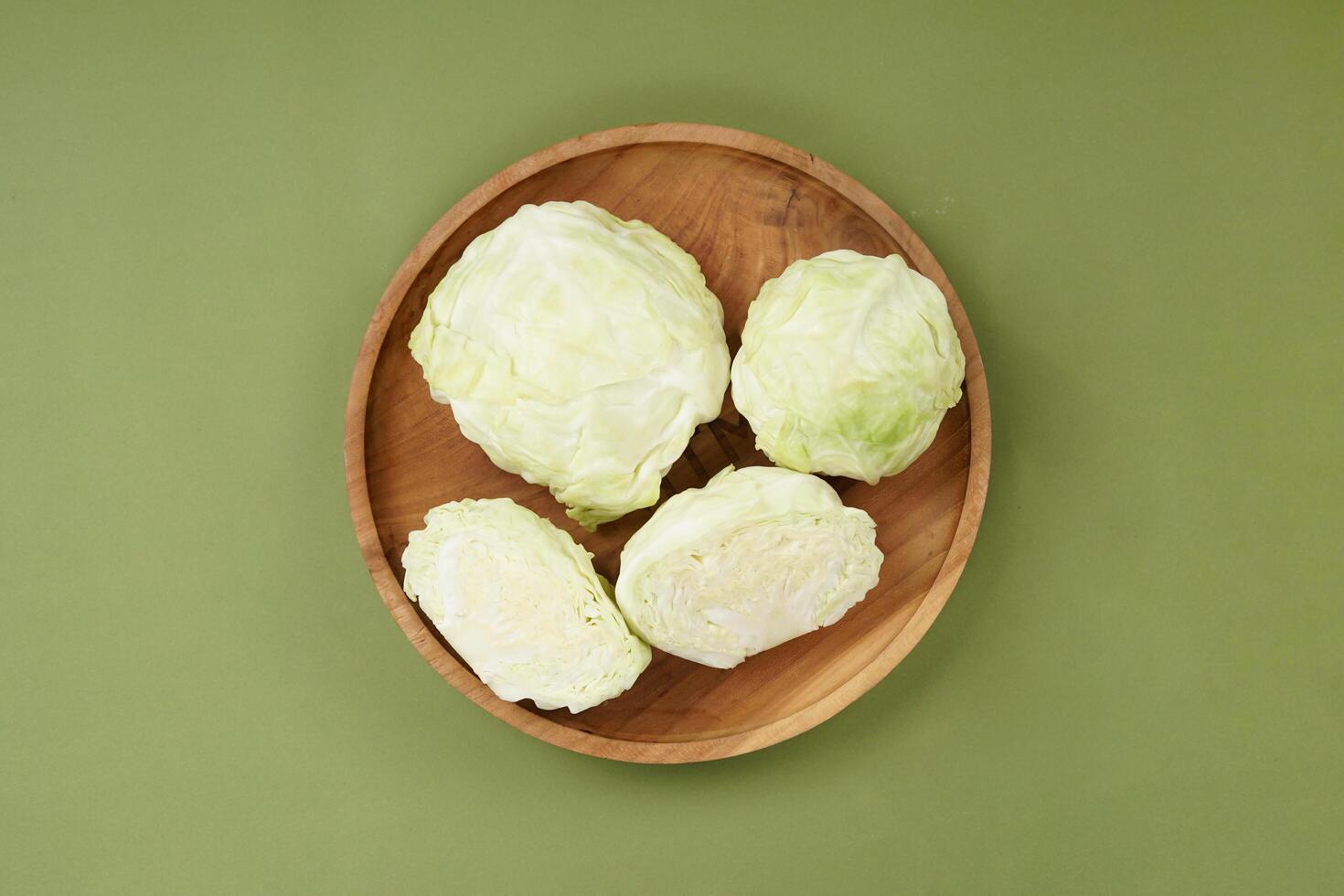 Green cabbage on a wooden plate, isolated against a green background, top view photo