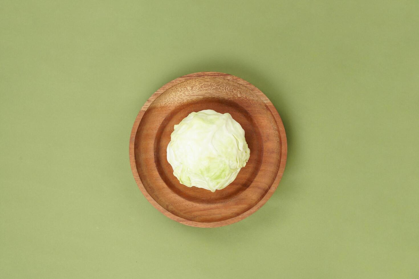Green cabbage on a wooden plate, isolated against a green background, top view photo