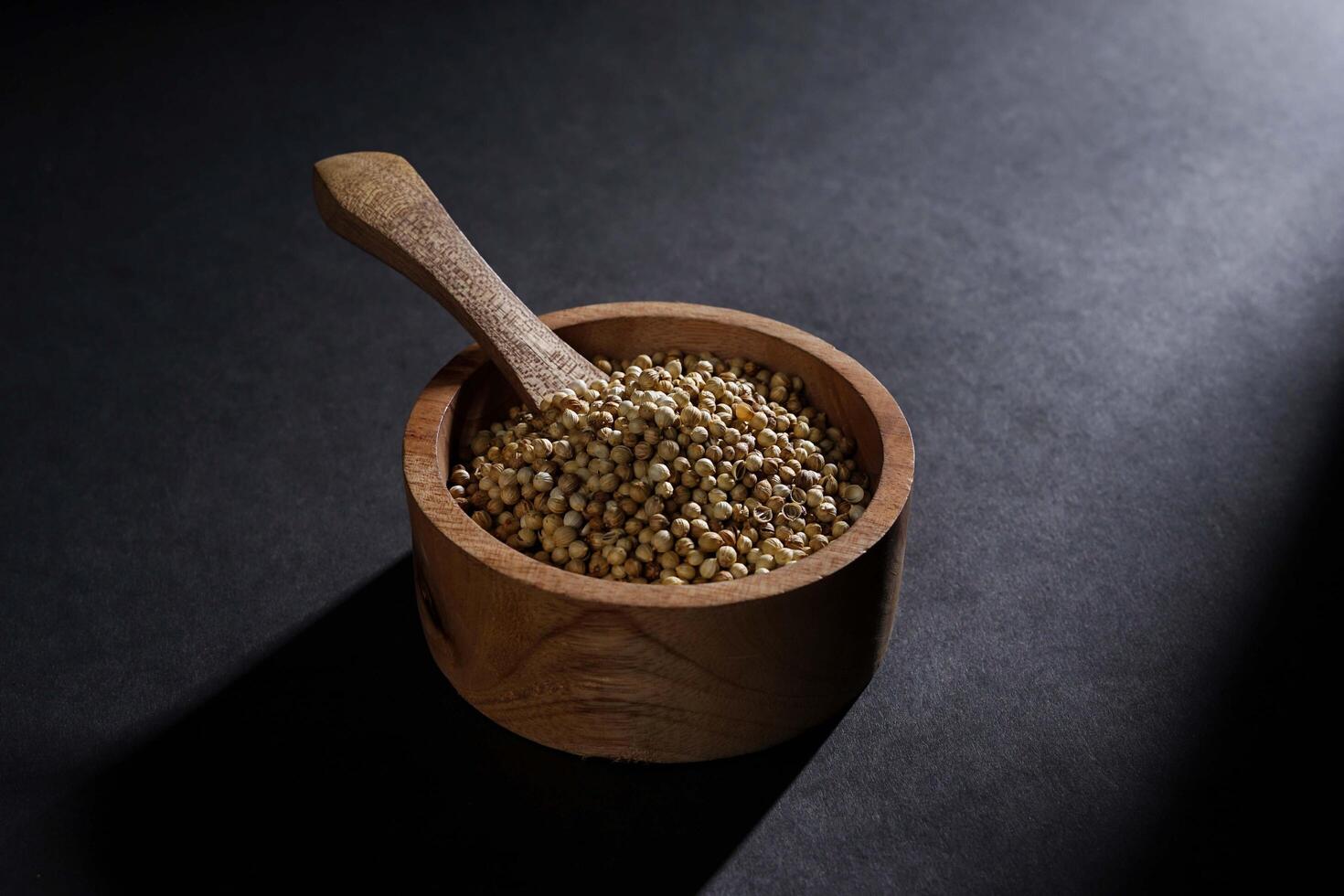 coriander seed in wooden bowl isolated on dark background, spice concept photo