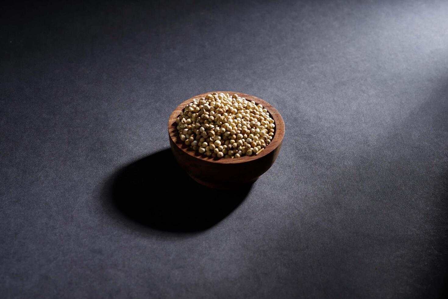 coriander seed in wooden bowl isolated on dark background, spice concept photo
