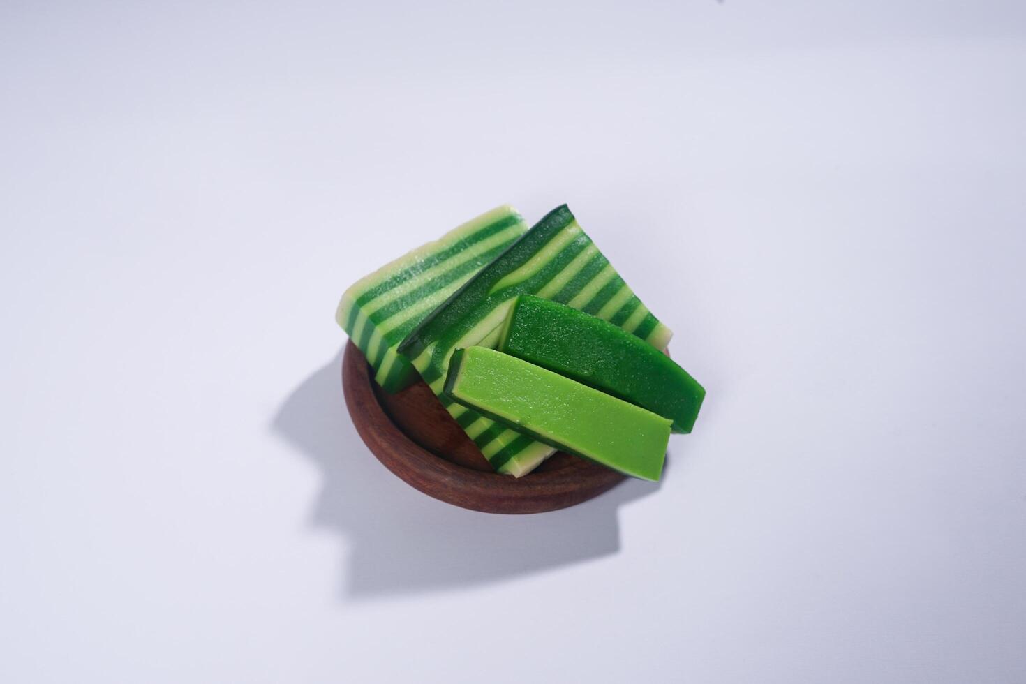 Sticky layer cake or Kue Lapis on wooden plate isolated on white background. Indonesian traditional dessert made from rice flour and coconut milk, steamed layer by layer served on banana leaves. photo