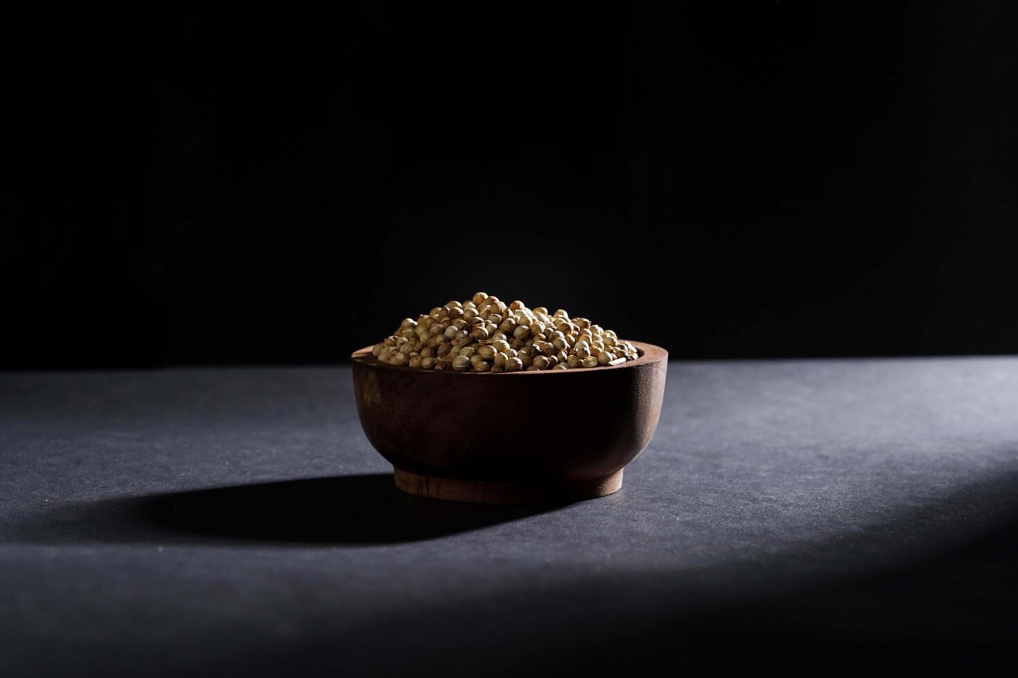 coriander seed in wooden bowl isolated on dark background, spice concept photo