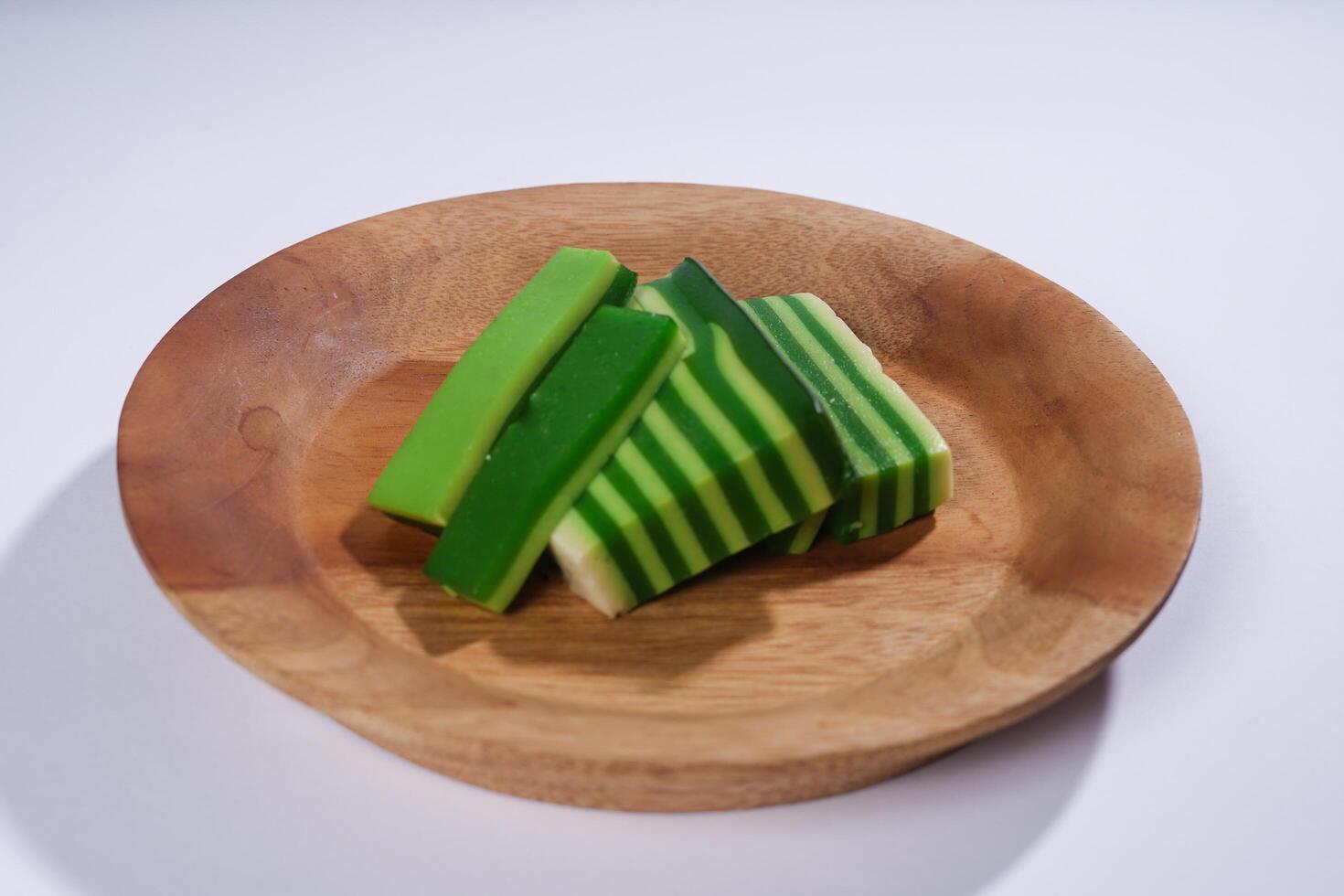 Sticky layer cake or Kue Lapis on wooden plate isolated on white background. Indonesian traditional dessert made from rice flour and coconut milk, steamed layer by layer served on banana leaves. photo