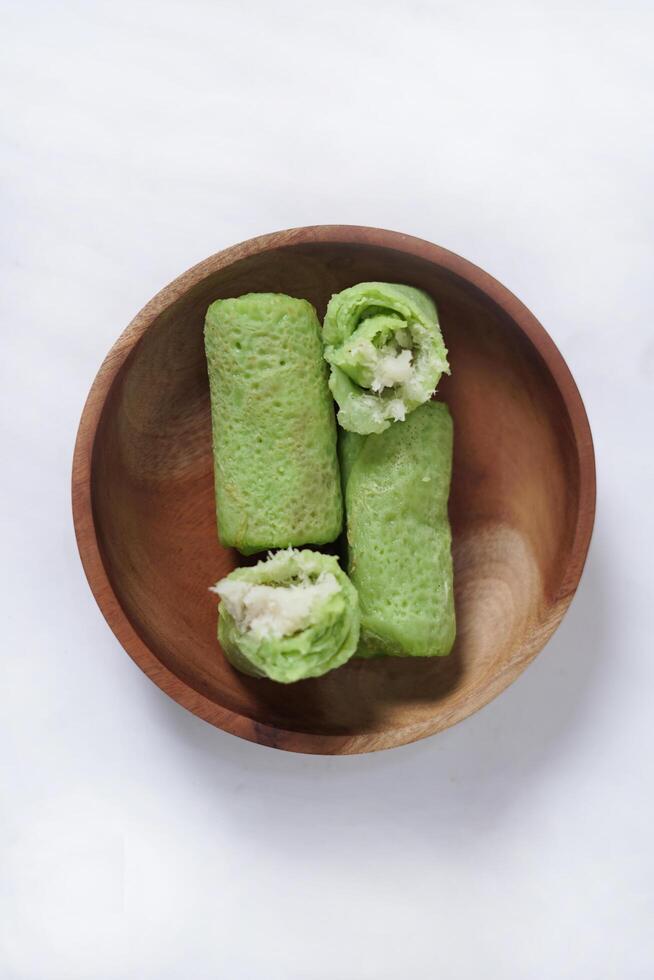 Traditional Indonesian food called 'Dadar Gulung' on a wooden plate, an elliptical cake filled with grated coconut and liquid palm sugar, Dadar gulung top view isolated on a white background. photo