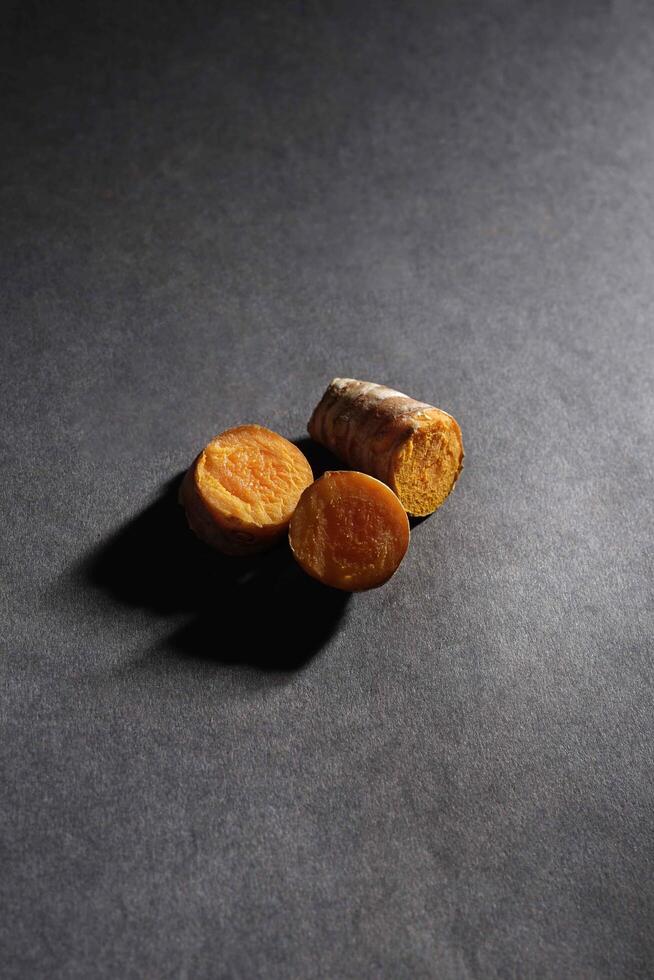 Fresh turmeric root and slices in wooden bowl isolated on dark background, turmeric Curcuma longa Linn, spice concept photo