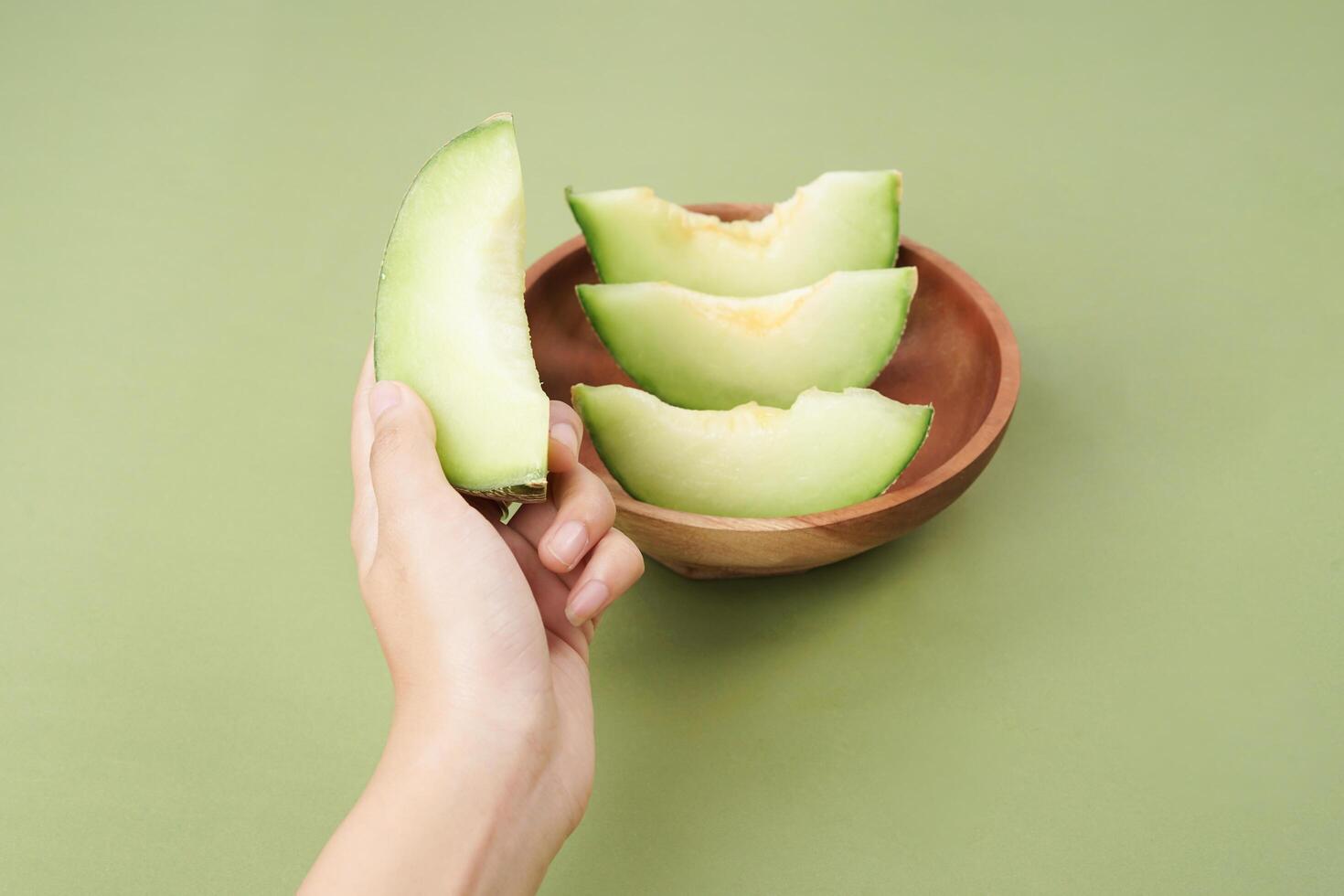 Green cantaloupe melon slice in wooden bowl isolated on green background, green melon photo