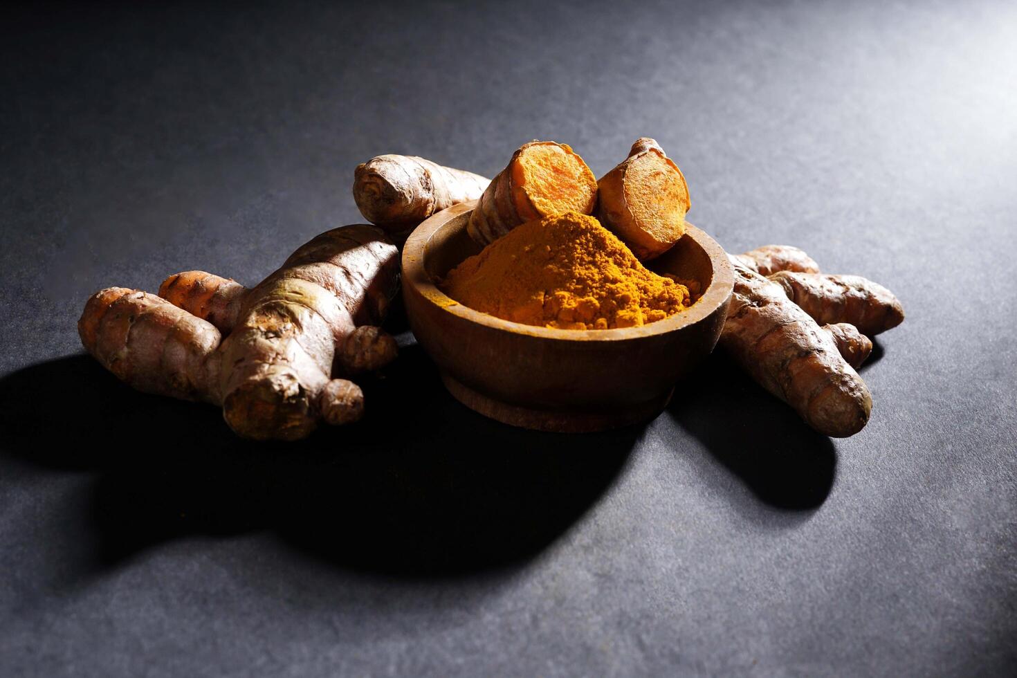 Fresh turmeric root and turmeric powder in wooden bowl, turmeric isolated on dark background, spice concept photo