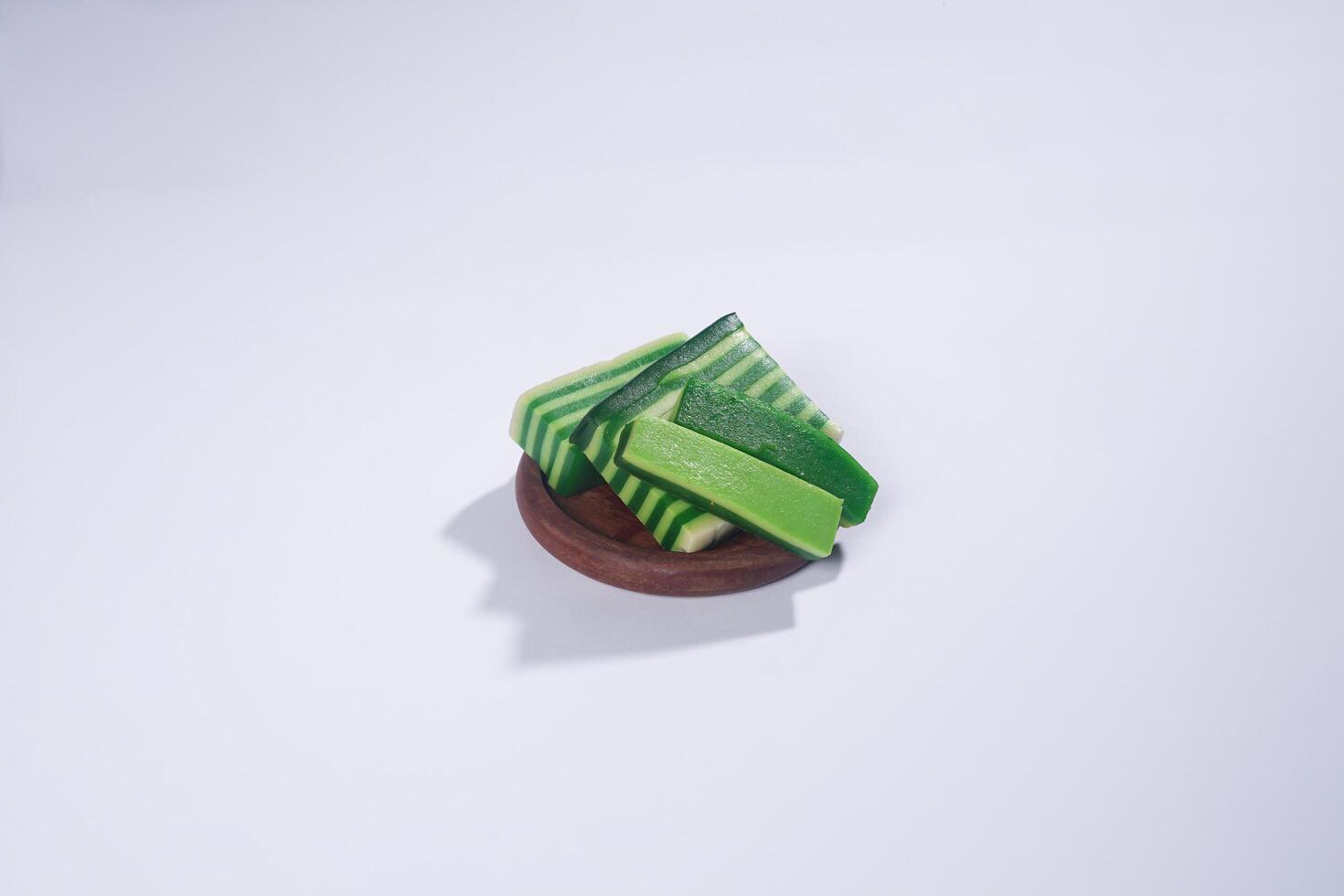 Sticky layer cake or Kue Lapis on wooden plate isolated on white background. Indonesian traditional dessert made from rice flour and coconut milk, steamed layer by layer served on banana leaves. photo