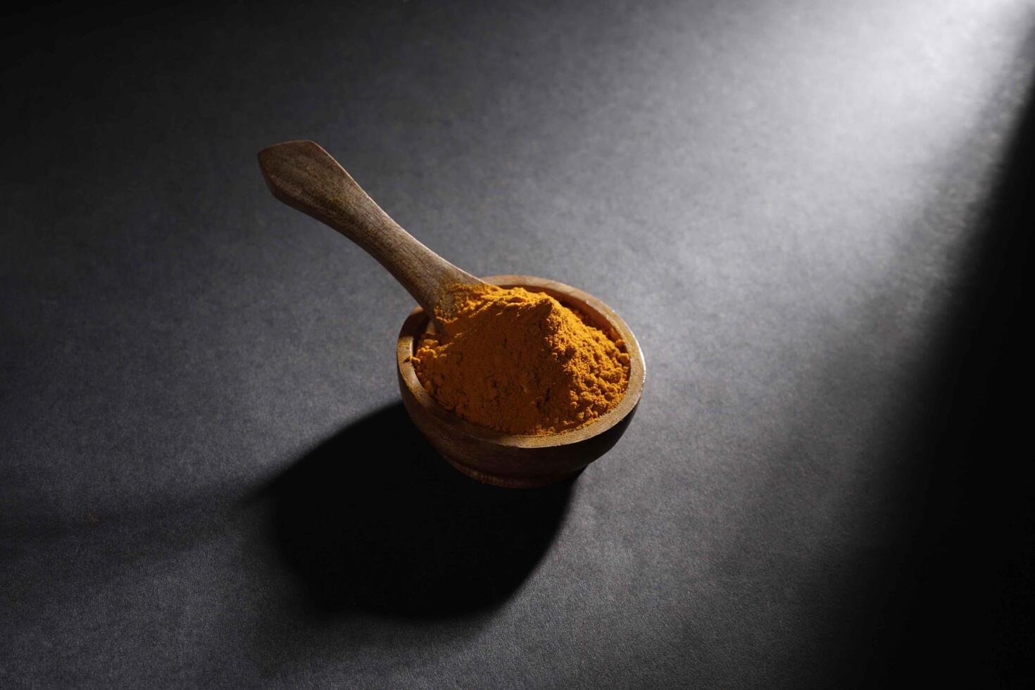 turmeric powder in wooden bowl isolated on dark background, turmeric Curcuma longa Linn, spice concept photo