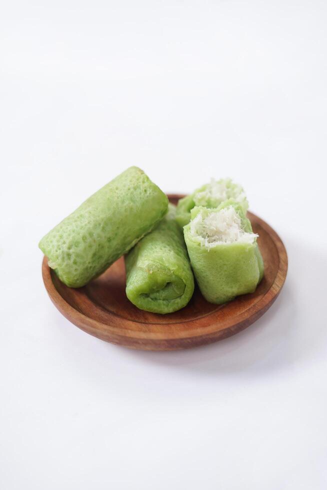 Traditional Indonesian food called 'Dadar Gulung' on a wooden plate, an elliptical cake filled with grated coconut and liquid palm sugar, isolated on a white background. photo
